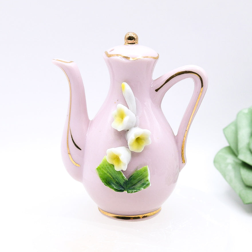 Pink ceramic teapot with floral designs on a white background