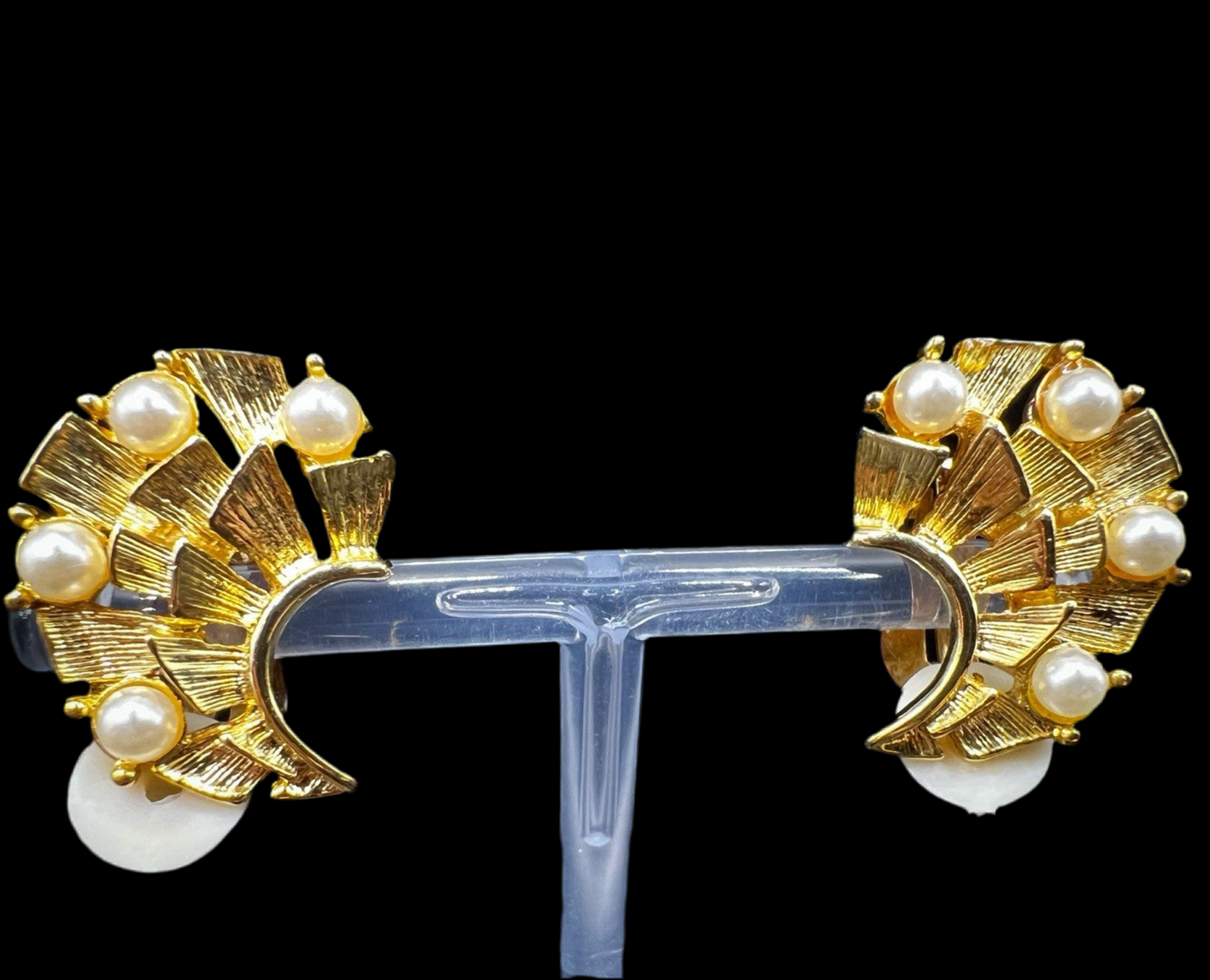 Pair of gold-tone fan earrings with pearl accents mounted on a transparent stand, showcasing the front design symmetrically.